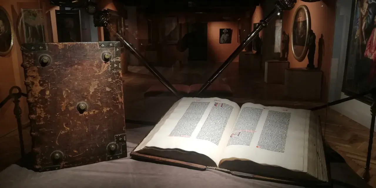 W muzeum diecezjalnym w Pelplinie eksponaty takie jak stary, oprawny księgozbiór i otwarta księga z tekstem przyciągają wzrok zwiedzających.