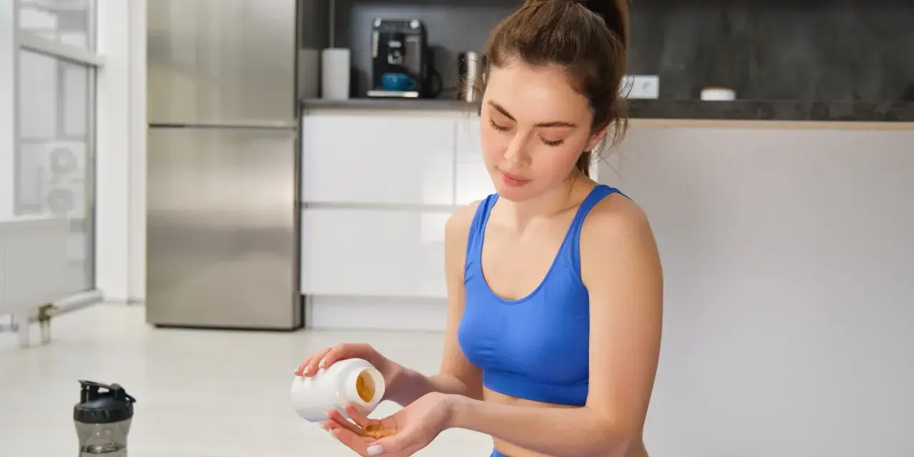 Femme en tenue de sport bleue prend des gélules, espérant un vitamine b12 effet immédiat pour son bien-être.