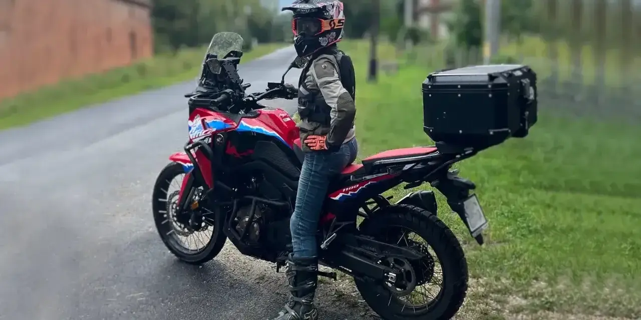 Motocyklistka w kasku i z kufrem na bagażniku gotowa na wyprawę po Kaszubach.