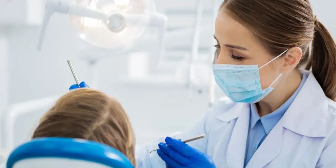 Dentystka bada uśmiech dziecka, by wykluczyć zapalenie dziąseł.