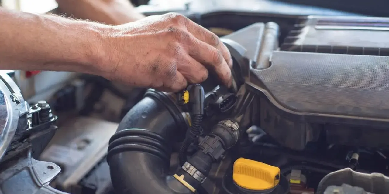 Ręce mechanika pracują przy silniku. Widoczny jest czarny przewód dolotowy i żółta zakrętka. p0101.