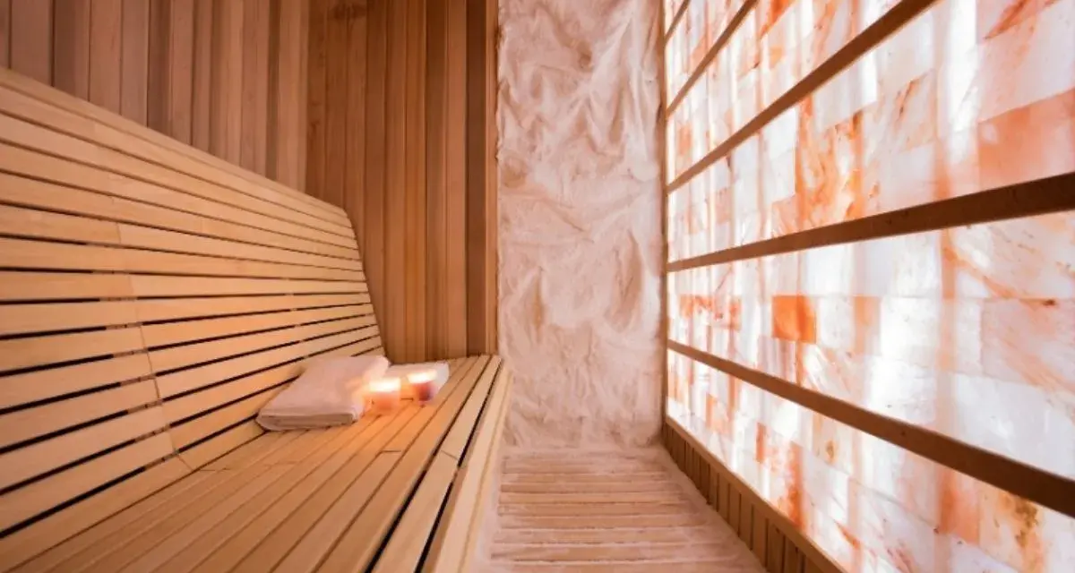 A serene salt sauna with a wooden bench, towels, candles, and a wall of glowing Himalayan salt bricks.