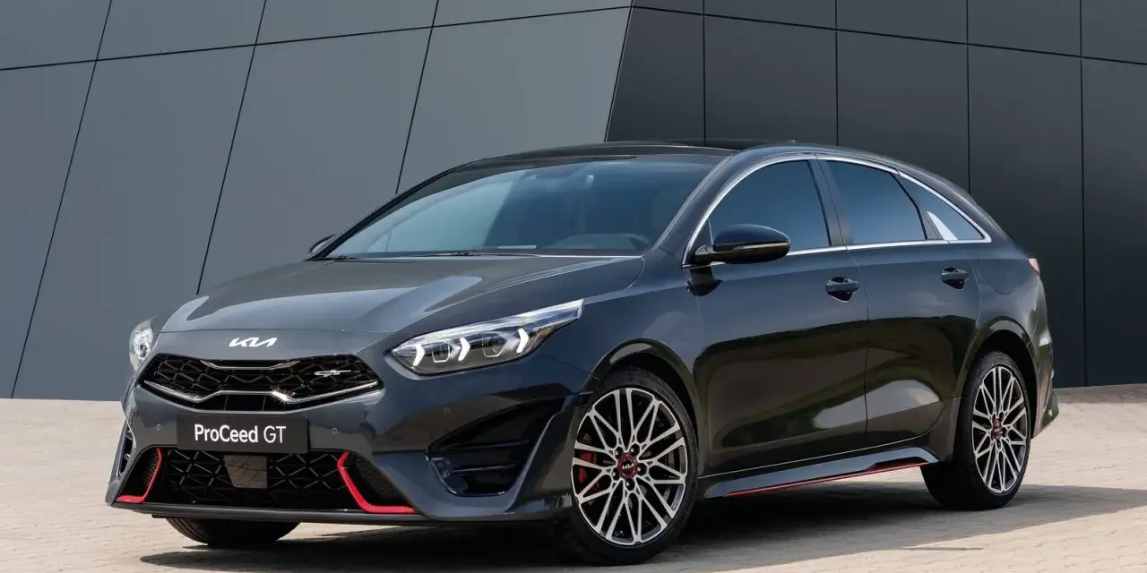 Stylowy, ciemnoszary Kia Proceed GT z czerwonymi akcentami i sportowymi felgami, zaparkowany przed nowoczesnym budynkiem.