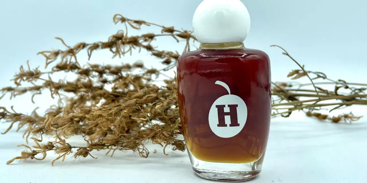 Frasco de aceite de hiperico con tapa blanca, junto a ramas secas.