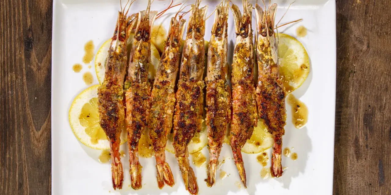 Gamberoni al forno dorati e croccanti, serviti su fette di limone e conditi con un sugo saporito.