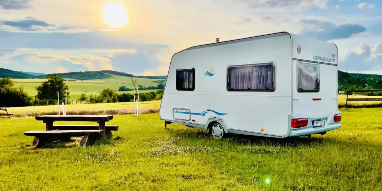 Przyczepa Caravelair zaparkowana na łące o zachodzie słońca. W tle malownicze wzgórza i pola.