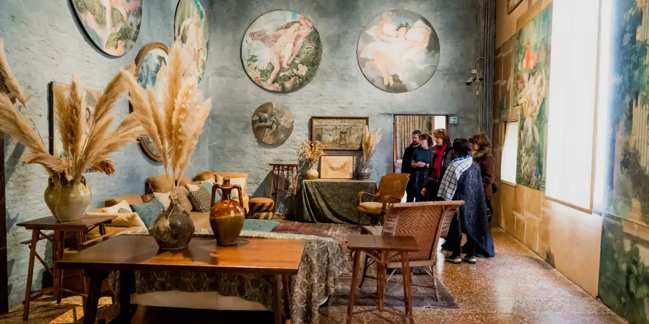 Interno del museo Palazzo Fortuny con opere d'arte alle pareti, arredi d'epoca e visitatori.
