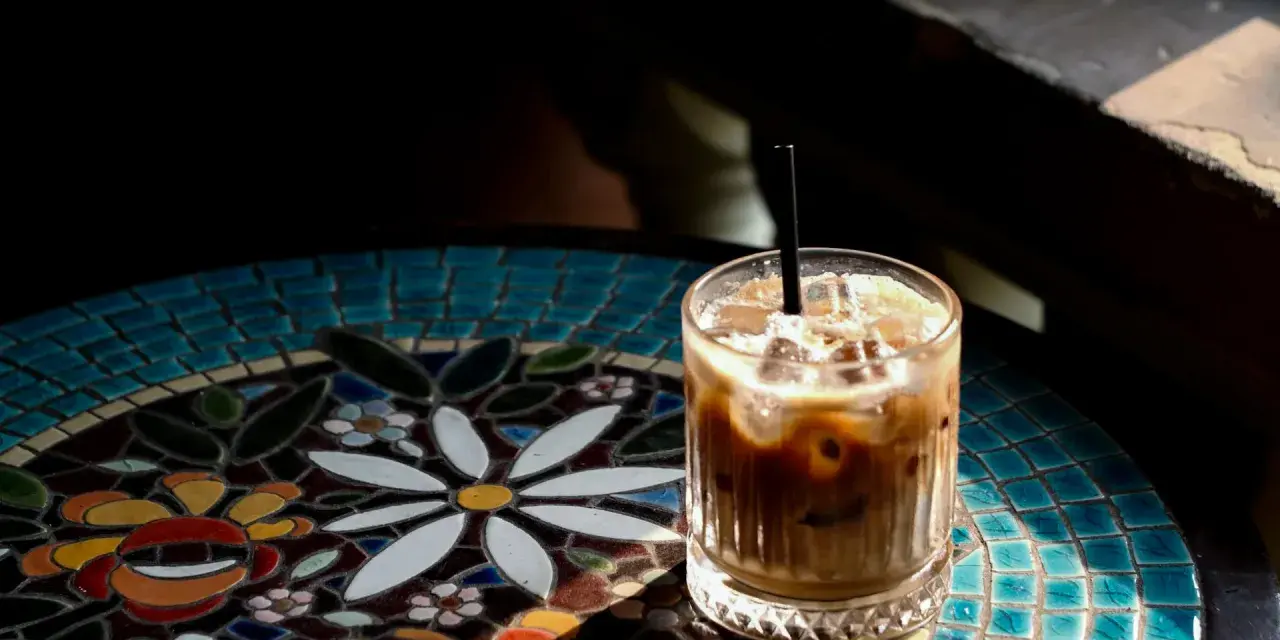 Orzeźwiający cold brew latte z lodem, podany na kolorowym, mozaikowym stoliku, w promieniach słońca.