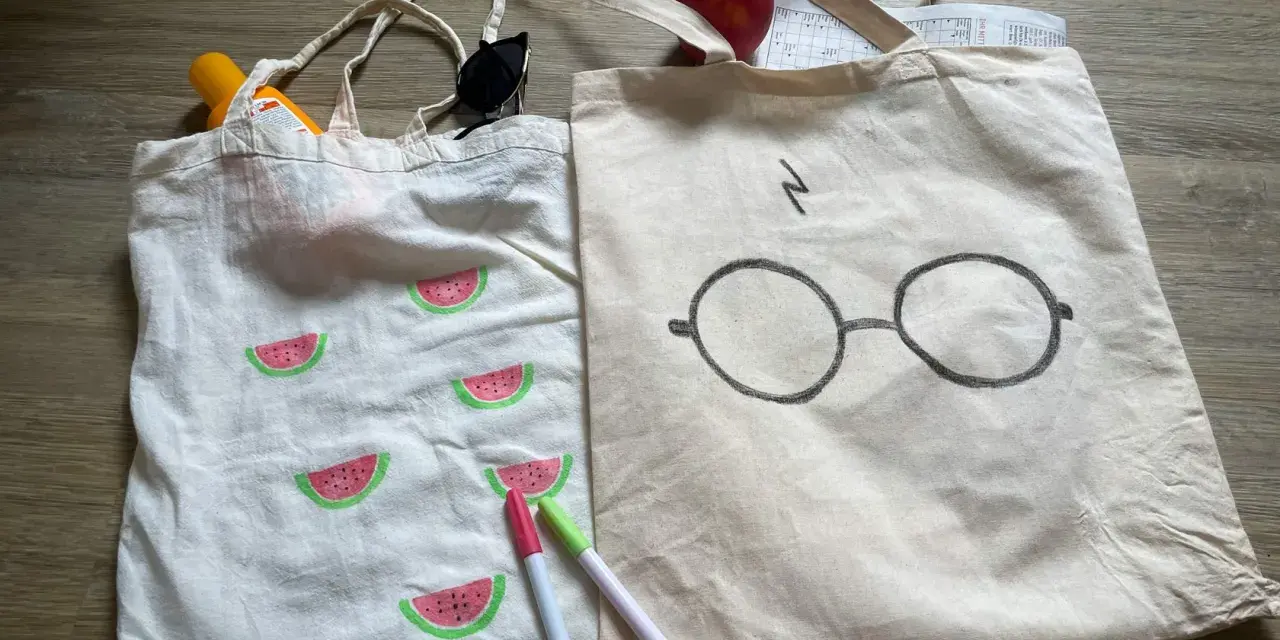 Zwei jute beutel bemalen: einer mit Wassermelonen, der andere mit Harry Potters Brille. Sonnencreme, Sonnenbrille und Stifte liegen daneben.