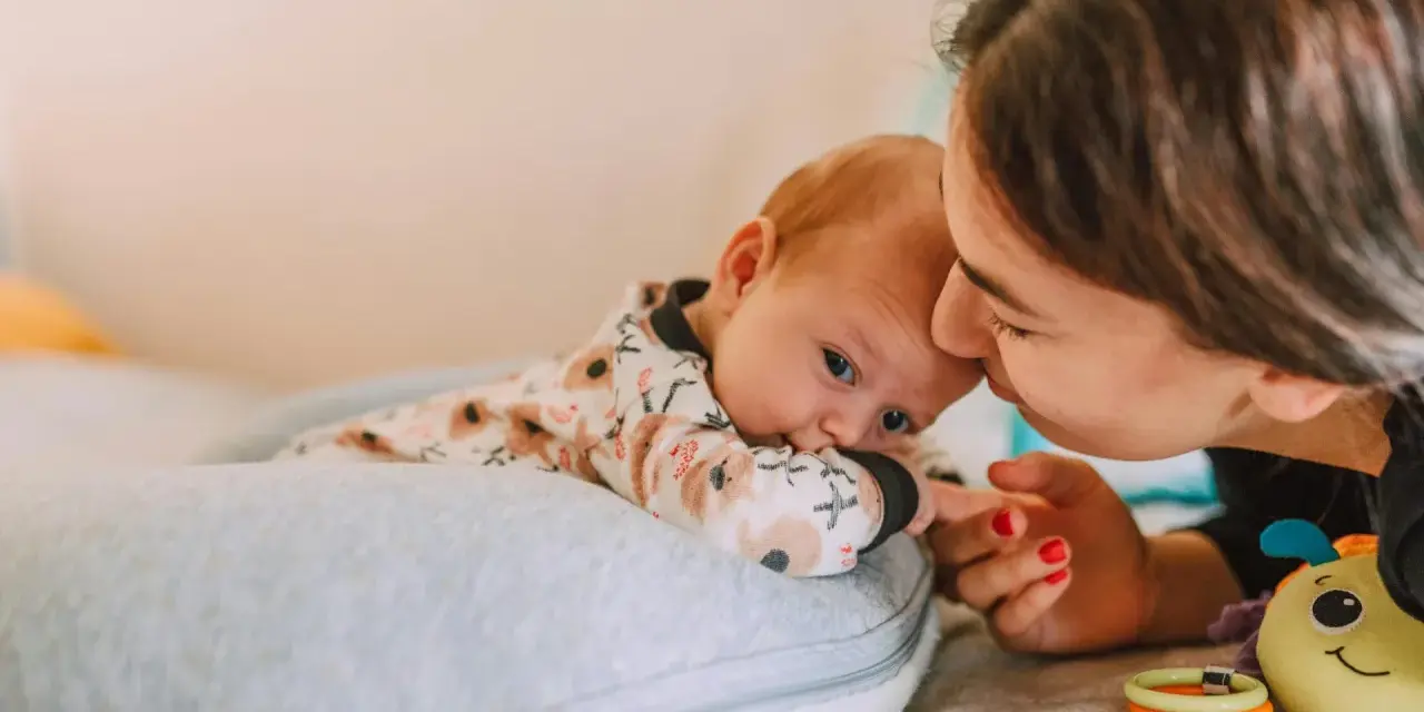 Mama pochyla się nad dzieckiem, które leży na poduszce. Szybki oddech u noworodka może być naturalny, ale czujność rodzica jest ważna.
