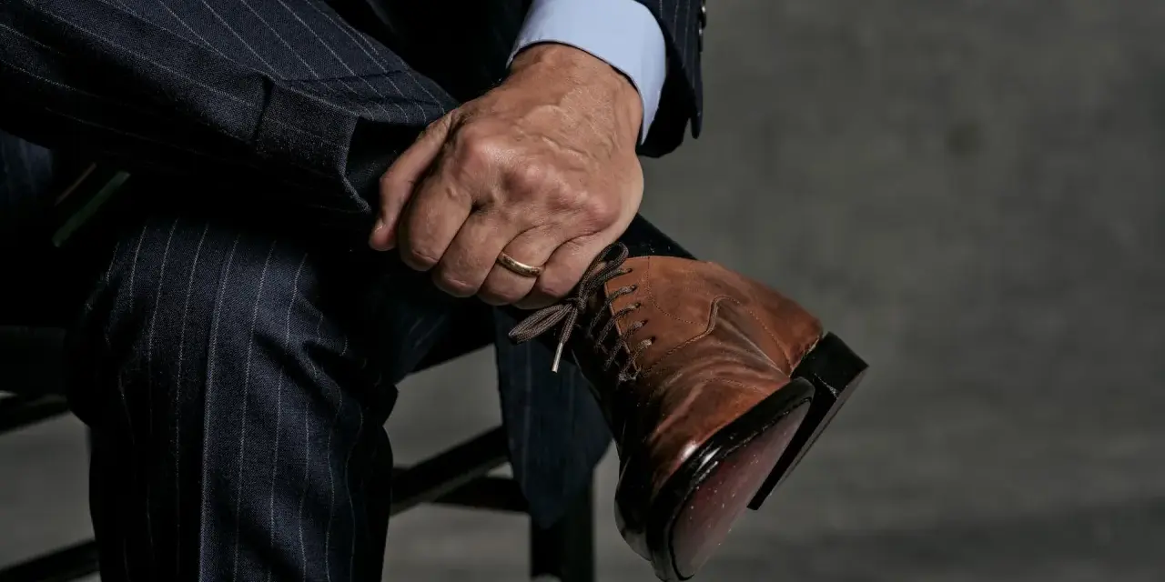 Un uomo con un abito gessato blu scuro e una camicia azzurra indossa eleganti scarpe stringate marroni.