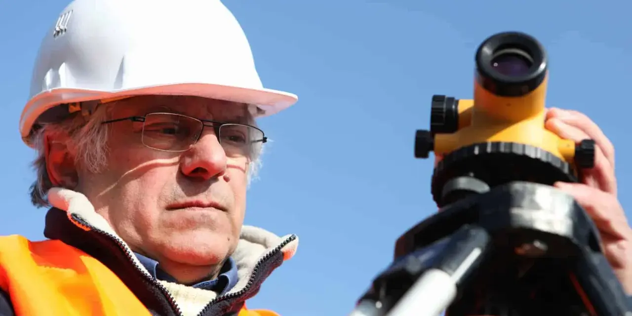Geodeta w kasku i kamizelce odblaskowej pracuje z niwelatorem. Zastanawiasz się, ile kosztuje geodeta przy budowie domu?