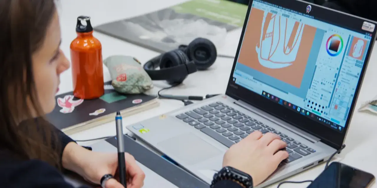 Studentka na studiach grafika Warszawa tworzy projekt na laptopie, używając tabletu graficznego.