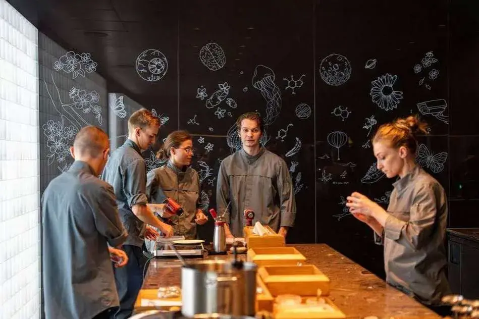 Une série de photos montrant une équipe en cuisine, devant un mur noir décoré de dessins scientifiques et floraux.