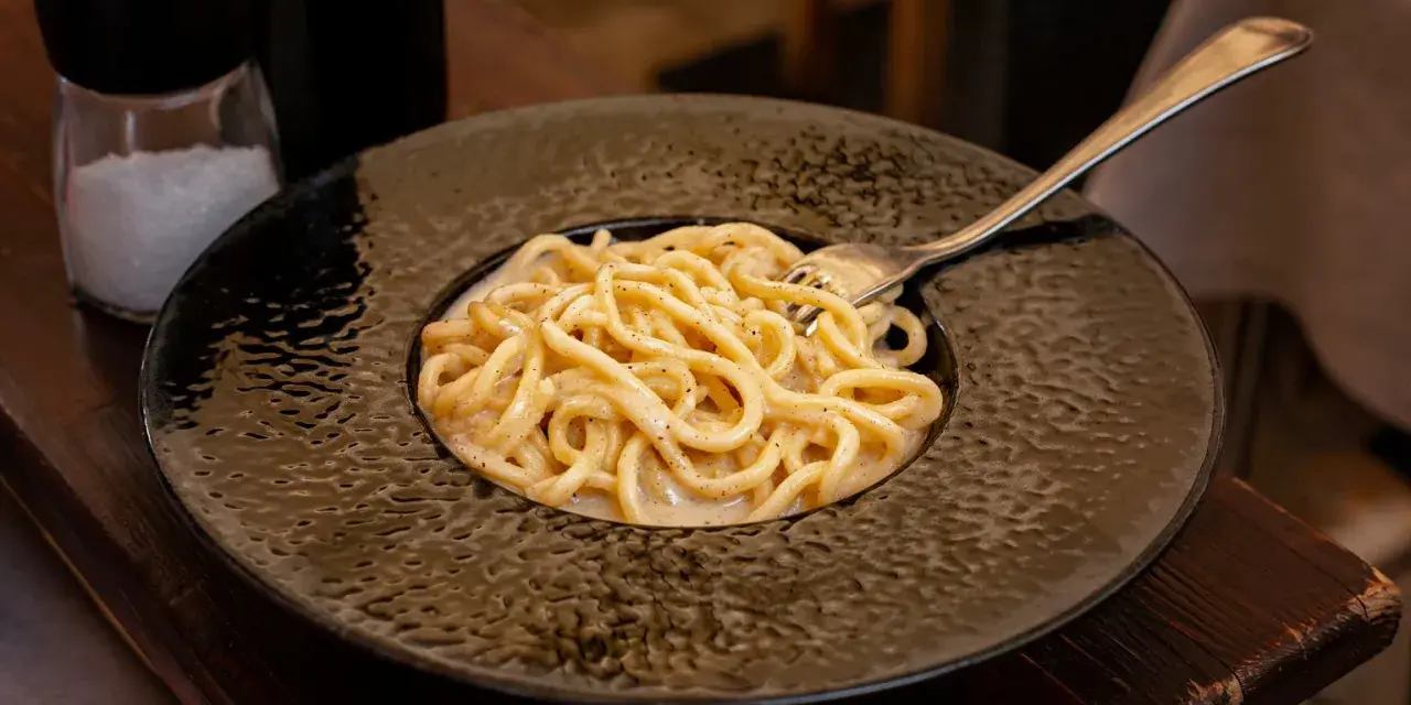 Pyszne cacio e pepe na czarnym talerzu, z widocznym młynkiem do pieprzu i solniczką w tle.