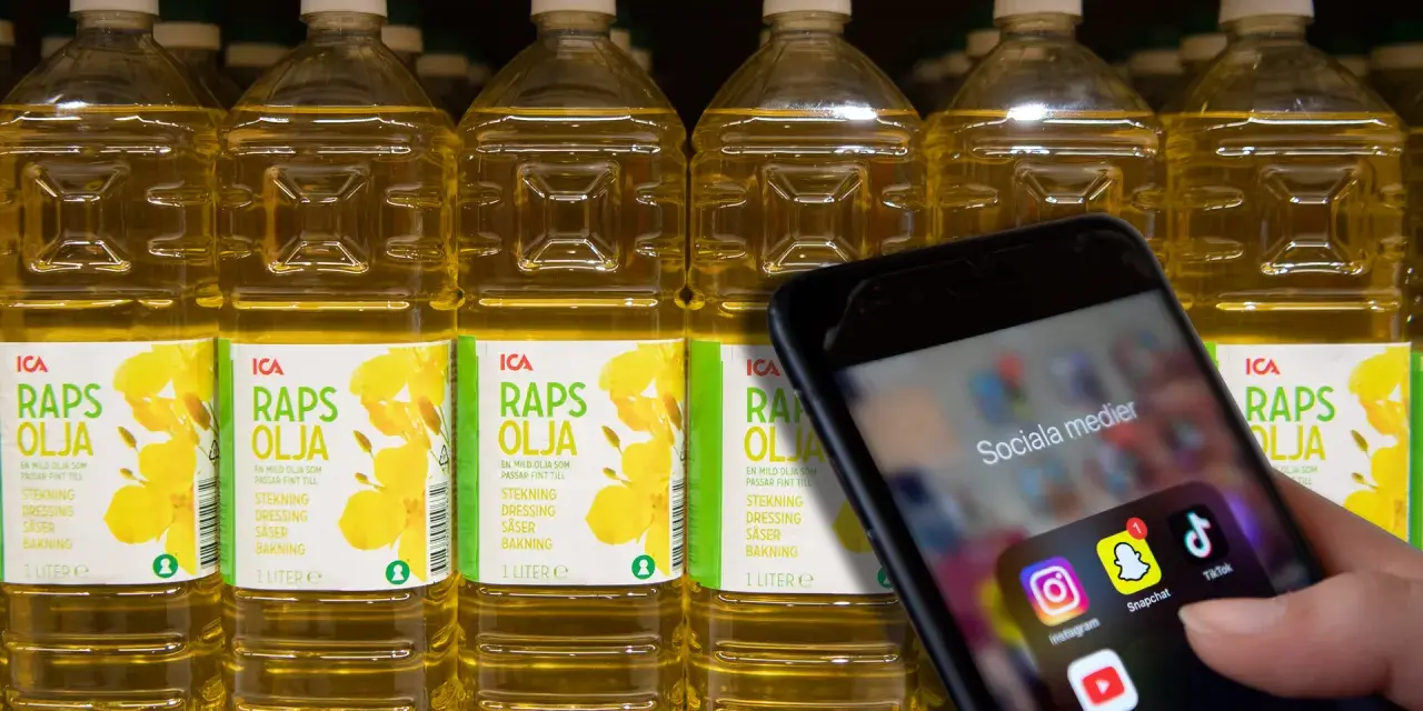 En hand håller upp en mobil med sociala medier-appar. Bakom syns rader av rapsoljeflaskor, där en del anser att rapsolja är farligt.