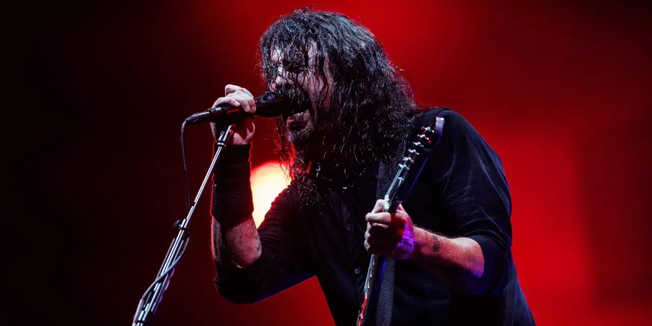Dave Grohl z Foo Fighters na koncercie, śpiewający do mikrofonu i grający na gitarze.