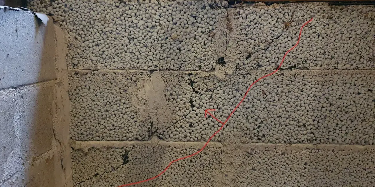 Synliga sprickor i grundmur av lättklinkerblock. En röd linje markerar en spricka som löper diagonalt över blocken.