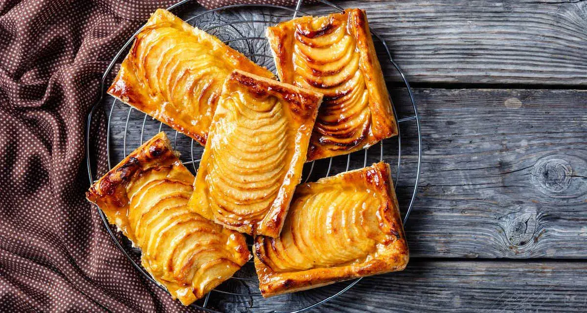 Deliziosi dolci con pasta sfoglia e mele caramellate, disposti su una gratella, su un tavolo di legno rustico.