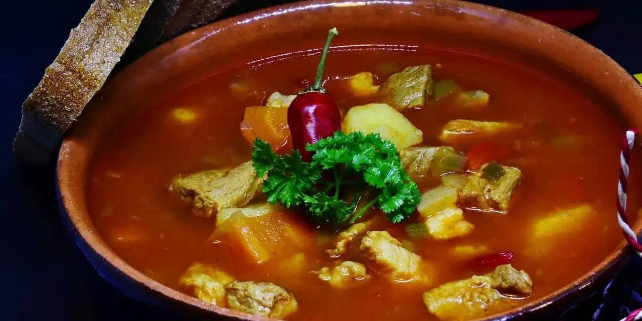 Pyszna zupa gulaszowa Ewy Wachowicz z kawałkami mięsa, ziemniaków i papryki, udekorowana papryczką chili i natką pietruszki. Podana z chlebem.