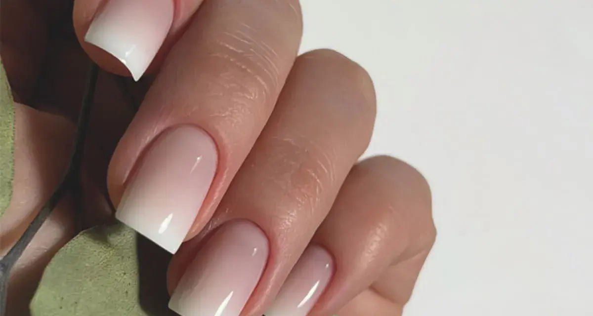 Mano con unghie curate e un effetto sfumato bianco e rosa, un esempio di nail art semplici ed eleganti.