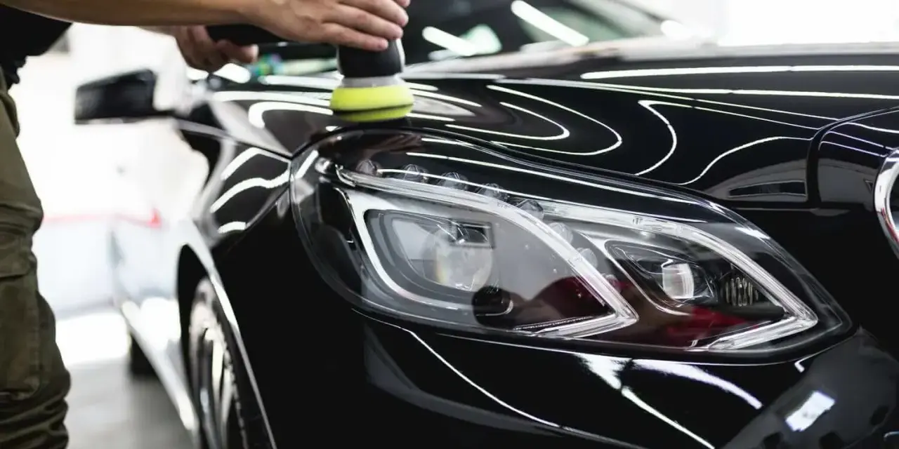 A person uses a polisher to wax a shiny black car, bringing out its deep gloss.