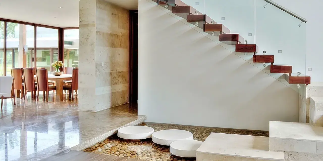Escalera de madera flotante con barandilla de cristal. Ideas para decorar una escalera de madera con un estanque de guijarros y piedras.