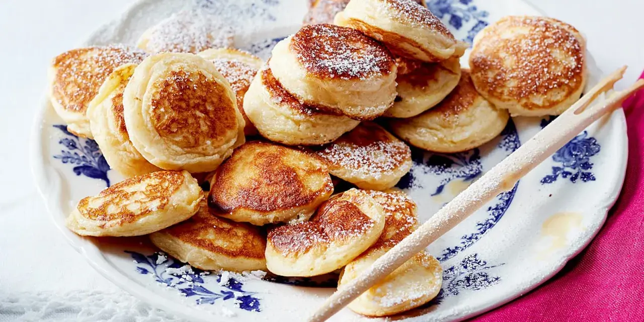 Ein Teller voller goldbrauner Poffertjes, bestäubt mit Puderzucker. Dieses Poffertjes Rezept ist ein Genuss!