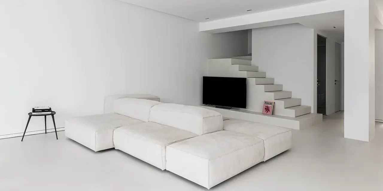Soggiorno minimalista con divano modulare bianco e pavimento in resina lucida. Scale moderne integrano la TV.