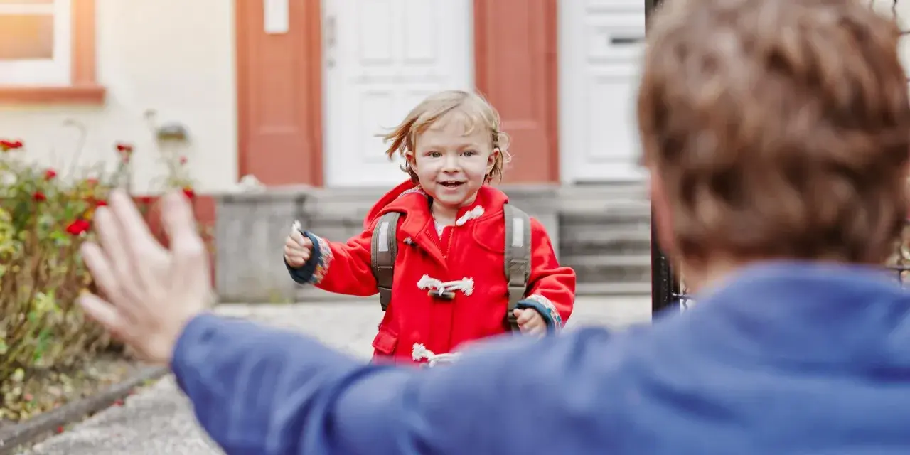 Kleines Mädchen im roten Mantel mit Rucksack rennt auf jemanden zu. Ein schönes Beispiel für das Wechselmodell bei Kindern.