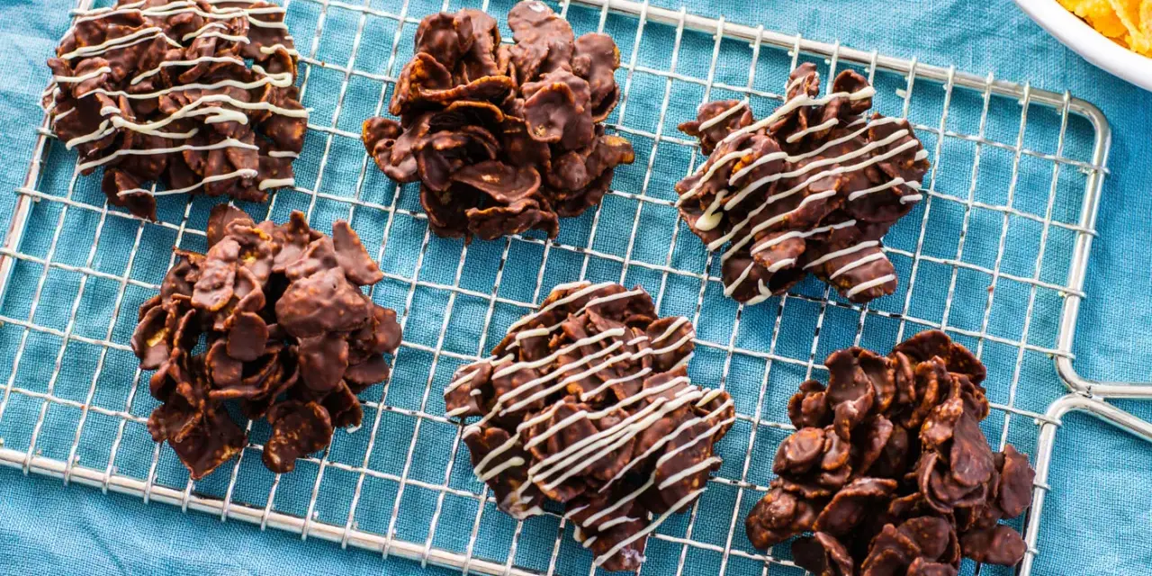 Sei dolcetti croccanti al cioccolato, simili a rose del deserto, raffreddano su una griglia. Alcuni sono decorati con sottili fili di cioccolato bianco.