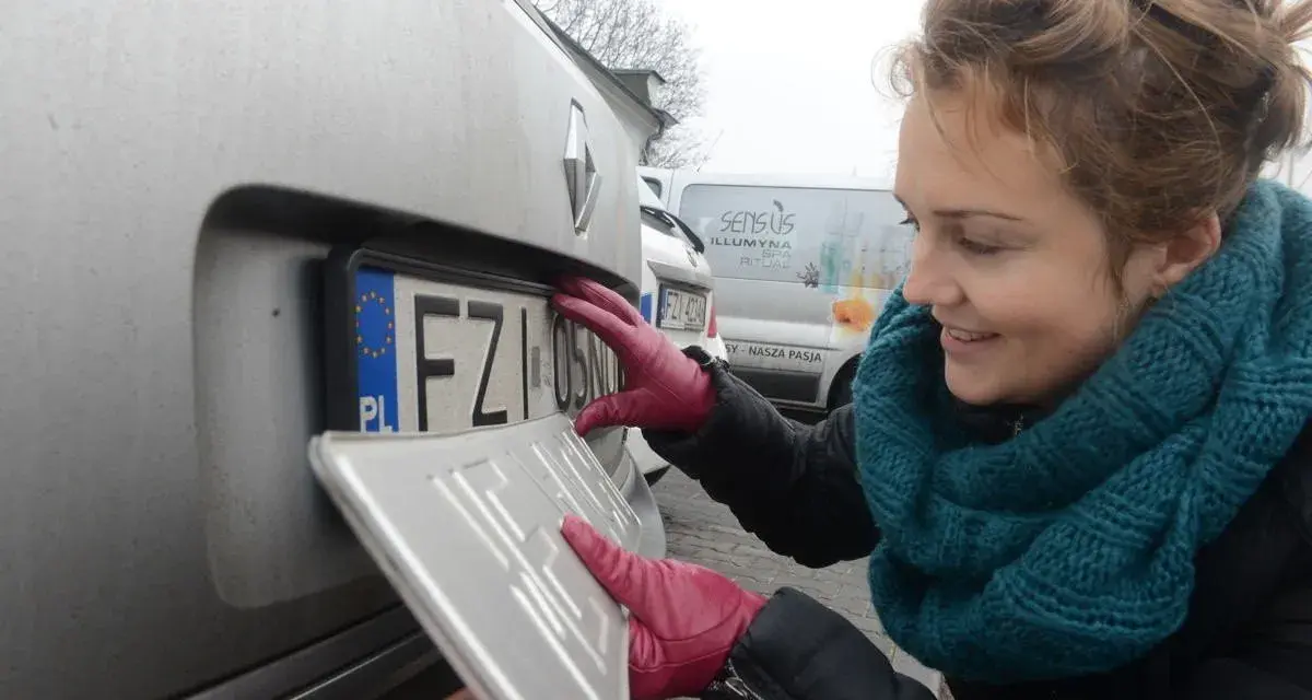 Kobieta w czerwonych rękawiczkach montuje tablicę rejestracyjną.