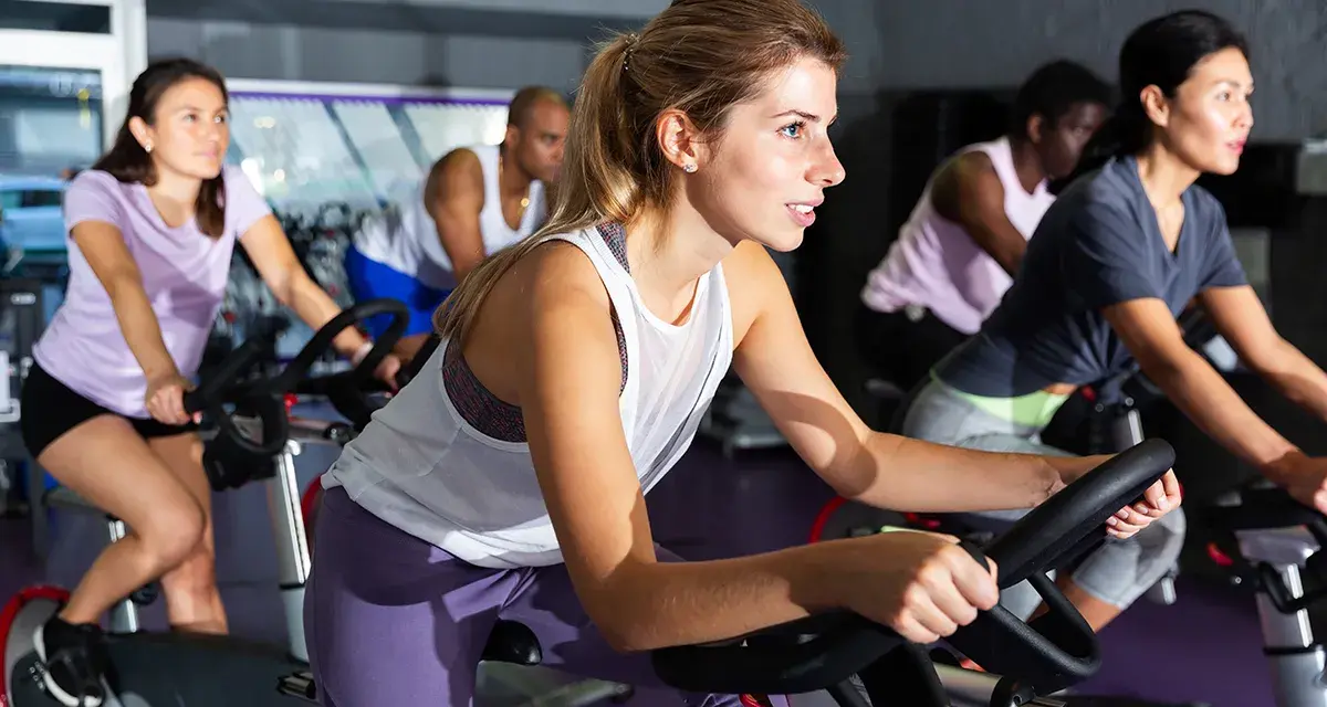 Women in a gym class experience the hiit cycling benefits, pedaling intensely on stationary bikes.