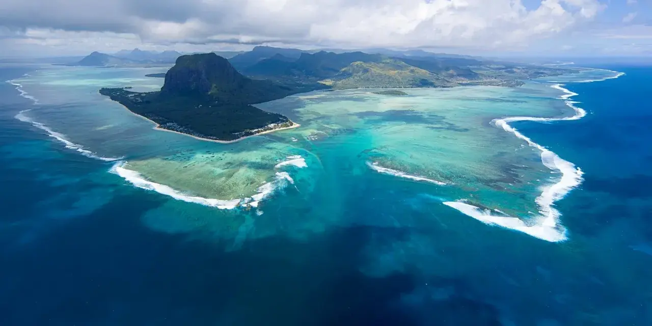 Majestatyczny Le Morne Brabant góruje nad turkusową laguną Mauritiusa. Woda mieni się odcieniami błękitu i zieleni, a białe fale rozbijają się o rafę.