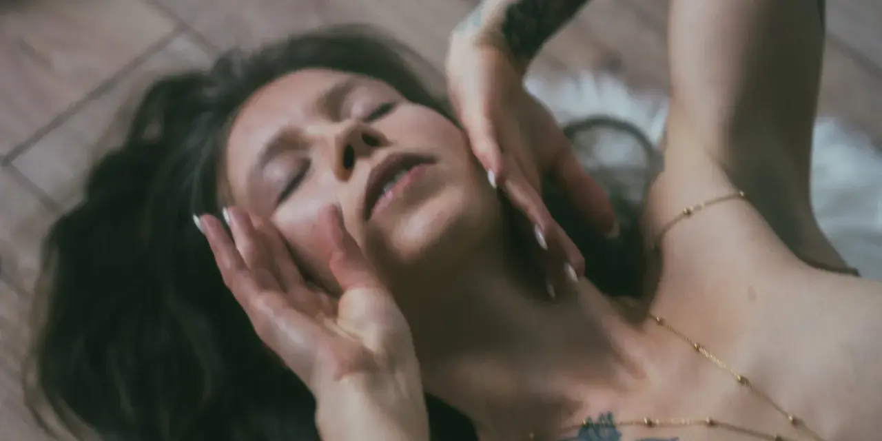 Lilith w lwie, z dłońmi na twarzy, w zmysłowym uścisku.