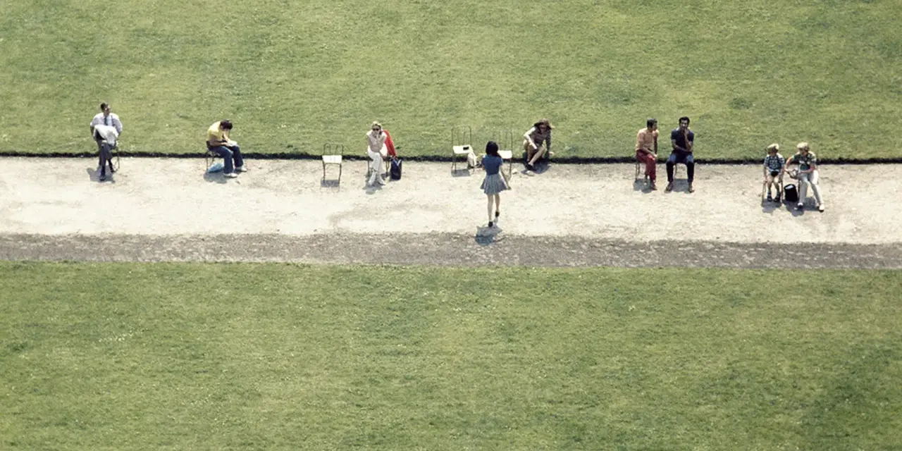 Luigi Ghirri uchwycił ludzi siedzących na krzesłach na tle zielonej trawy.