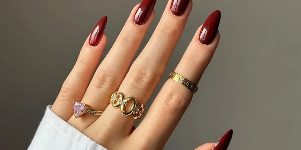 Main d'une femme aux ongles longs et pointus, vernis d'un profond couleur vernis automne. Bagues dorées ornées de pierres et de motifs.