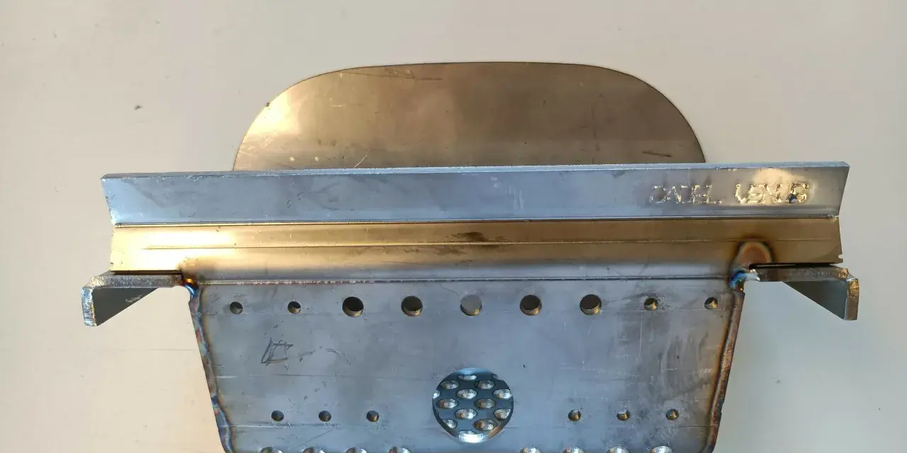 Un abbattitore di fumi per stufe a pellet, realizzato in metallo, con fori e un'area traforata.