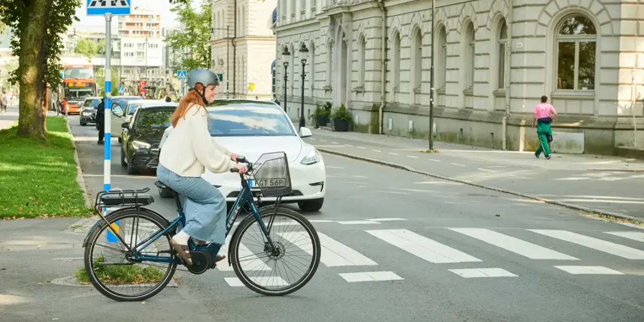 Kvinna på elcykel korsar övergångsställe. Trafik och byggnader i bakgrunden. Elcykel regler är viktiga för säkerheten.