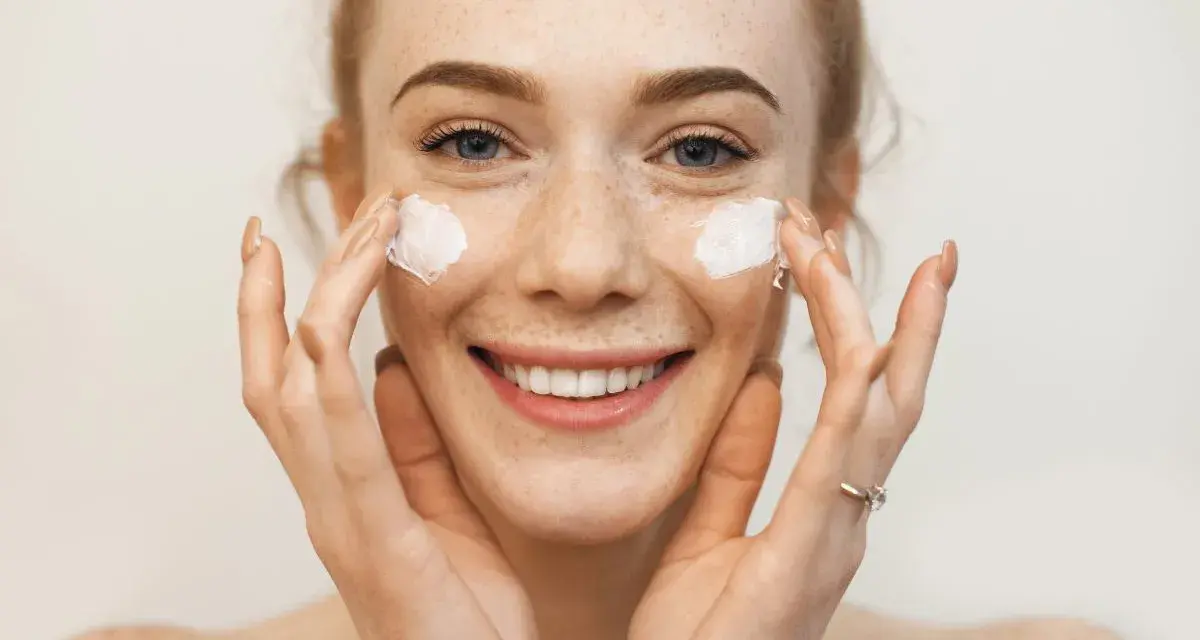 Uśmiechnięta dziewczyna z piegami nakłada krem na twarz. Sudocrem na co? Na suchą skórę, podrażnienia, zaczerwienienia.