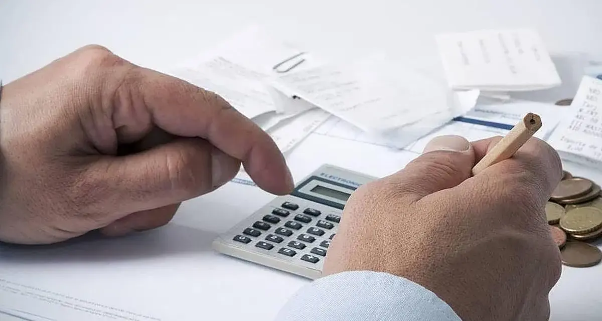 Manos calculando con calculadora y lápiz, rodeado de recibos y monedas. ¿Qué significa grupo de cotización 10?