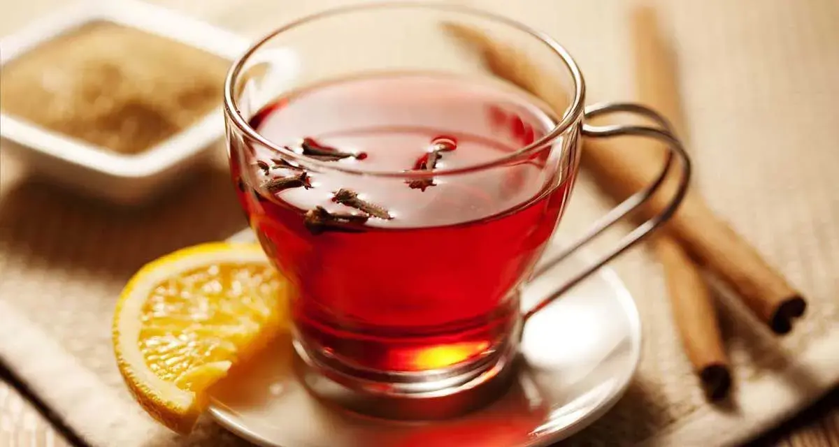 Té rojo con clavo y naranja, ideal para disfrutar de sus propiedades. Azúcar y canela al lado.