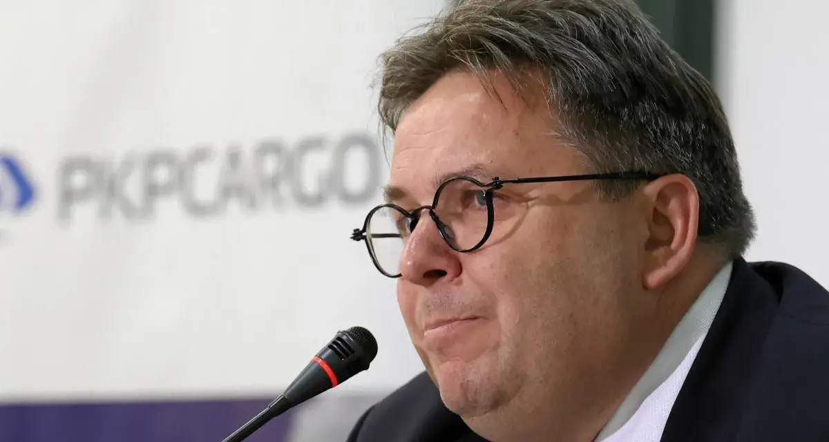 Mężczyzna w okularach przed mikrofonem na tle logo PKP Cargo.