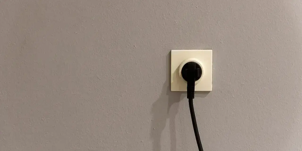 Gniazdko elektryczne z wtyczką na szarej ścianie. Czy to symbol energa taryfa urzędowa?