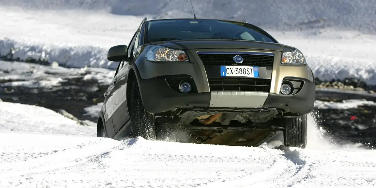 Un'auto con gomme invernali neve affronta un pendio innevato, sollevando spruzzi di bianco.