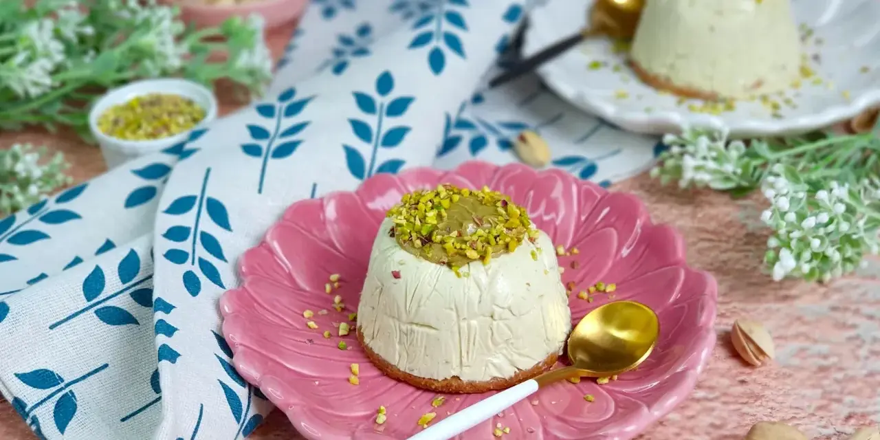 Delizioso semifreddo al pistacchio, guarnito con crema e granella di pistacchi, servito su un piatto rosa.