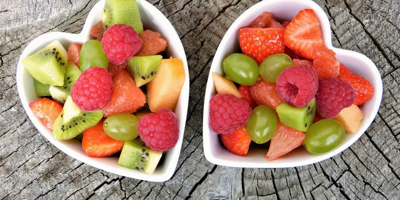 Dwa sercowate talerzyki pełne kolorowych, pokrojonych owoców: truskawek, malin, kiwi, winogron i grejpfruta. Idealne zdrowe przekąski dla dzieci.