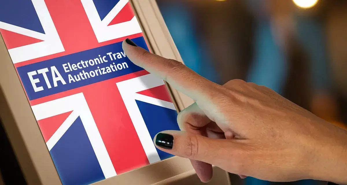 Palec dotyka ekranu z napisem ETA Electronic Travel Authorization i flagą Wielkiej Brytanii. Zastanawiasz się, ile kosztuje ETA do UK?