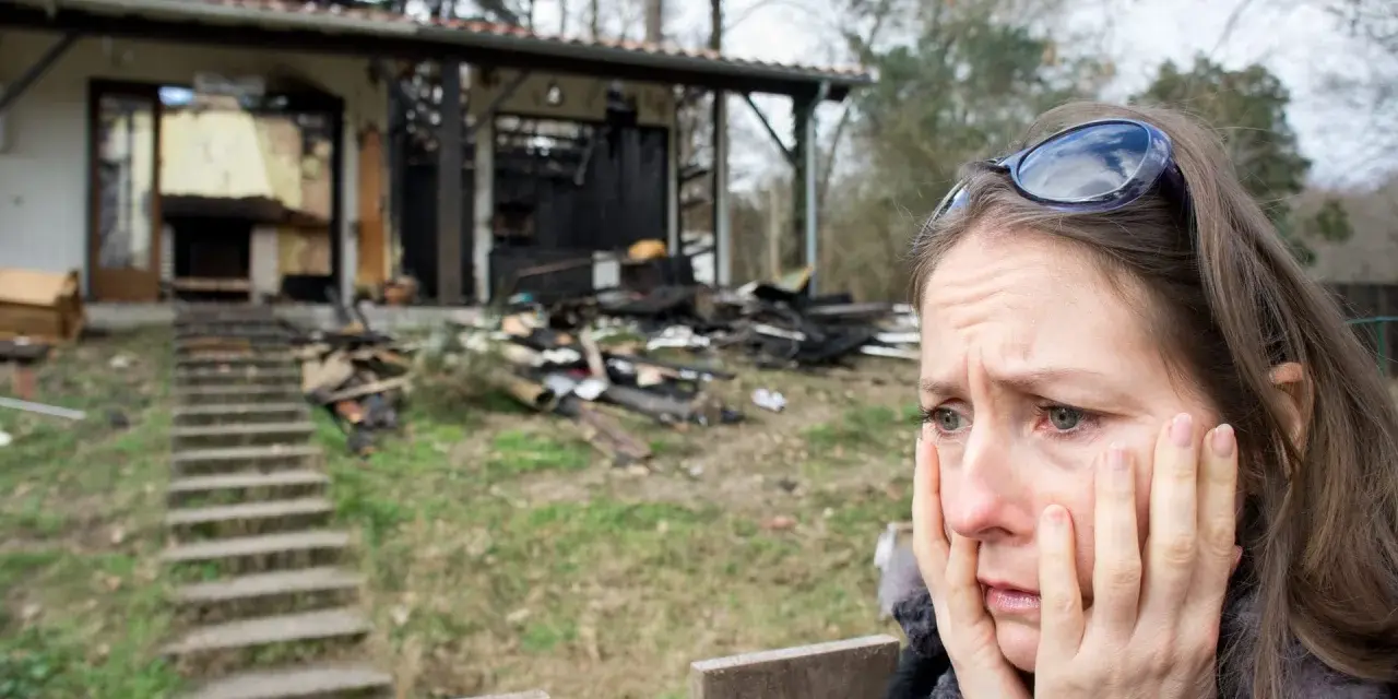 Verzweifelte Frau vor ihrem abgebrannten Haus. Die Versicherung zahlt nicht, ihr Leben liegt in Trümmern.