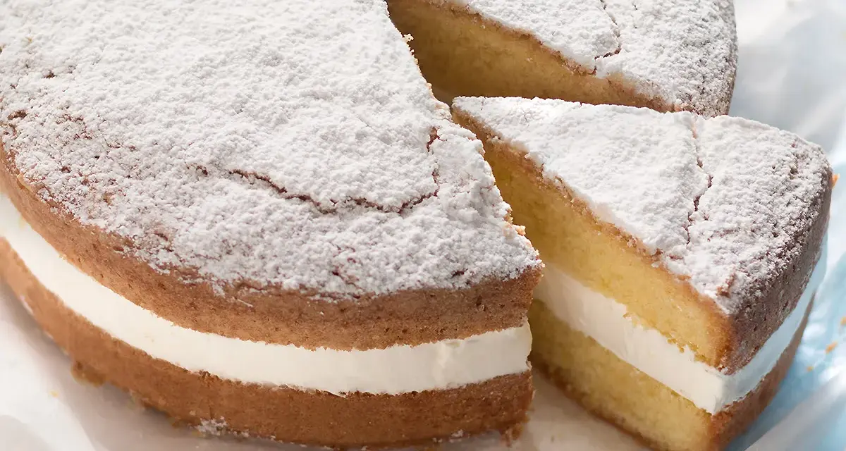 Torta paradiso sofficissima, con crema bianca e zucchero a velo. Una fetta è stata tagliata, invitando a gustarla.